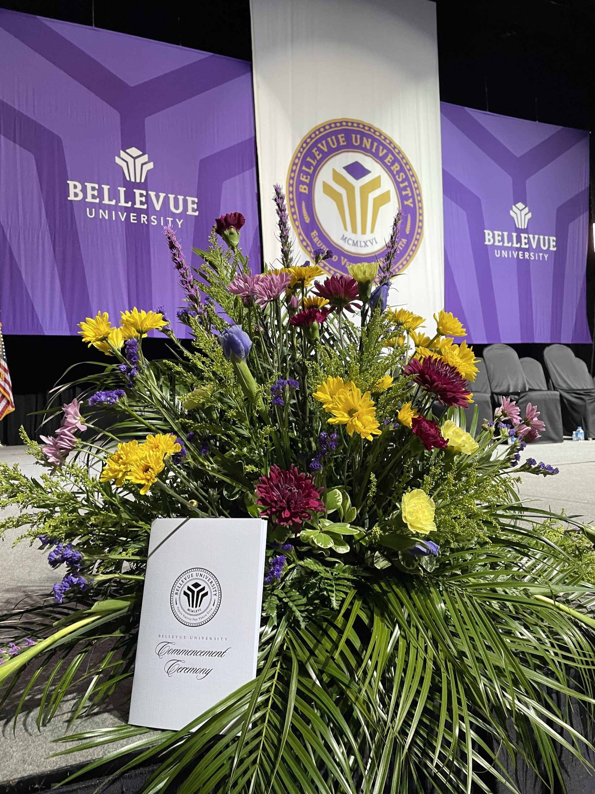 Commencement program and flowers in front of the Bellevue University commencement stage.