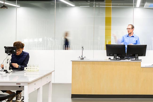Man teaching in lab and student looking in microscope