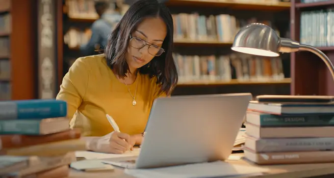 Woman wearing glasses in library with a computer.