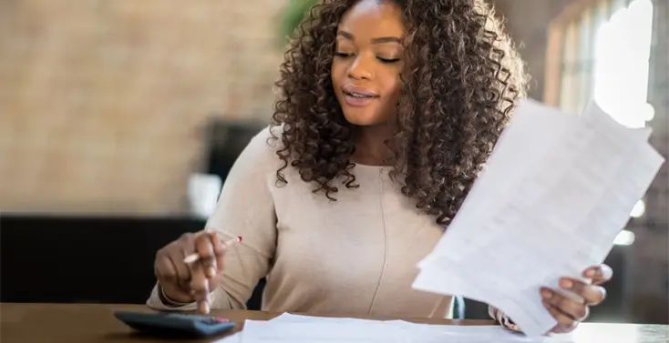 Female holding papers looking at a calculator.