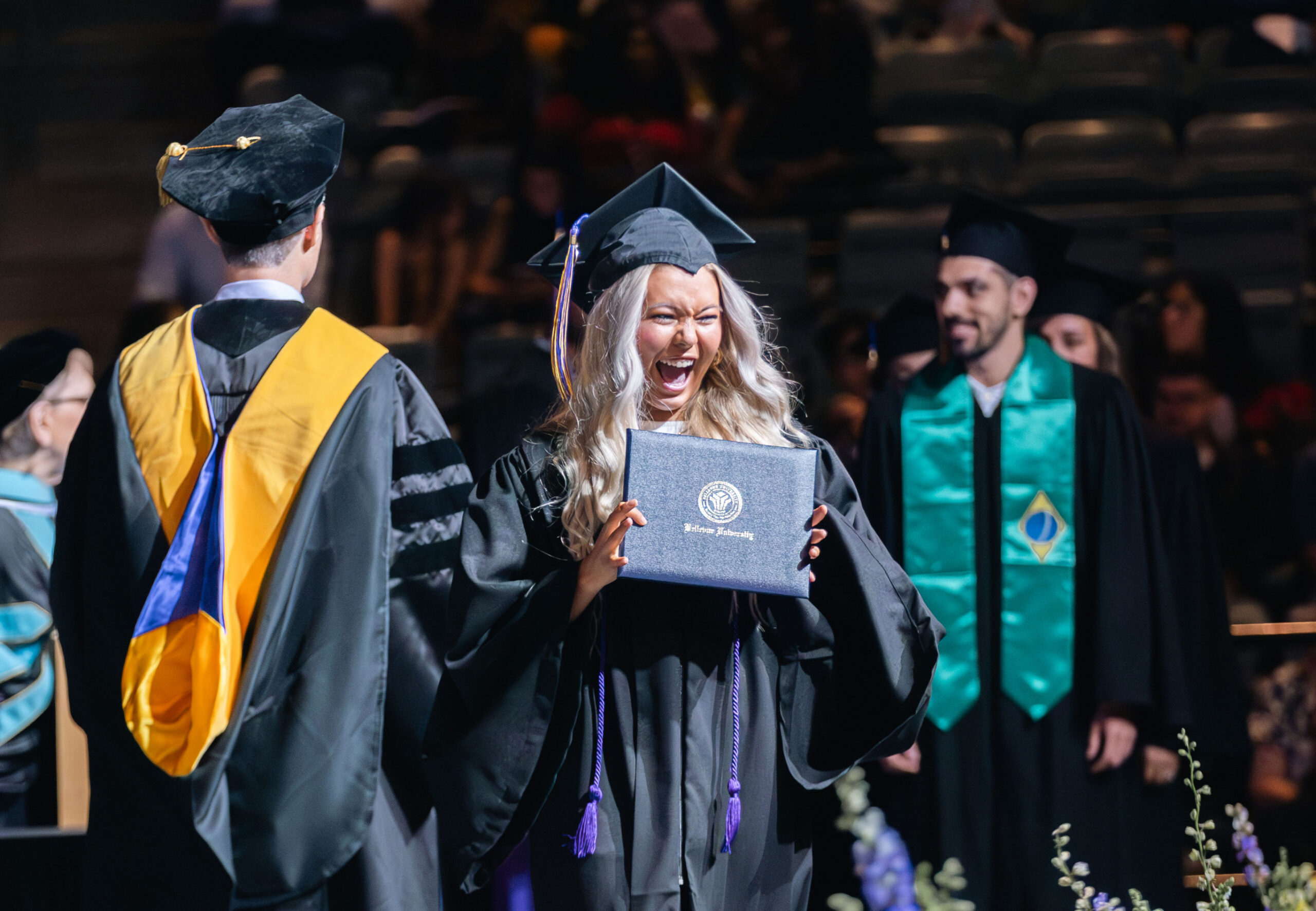 Woman in cap and gown smiling as she receives her diploma.
