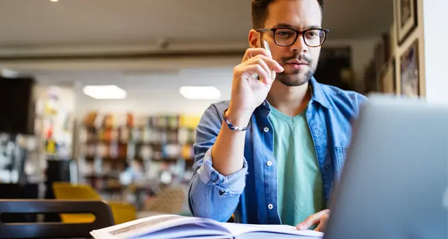 Man with glasses looking at a computer and an open book.