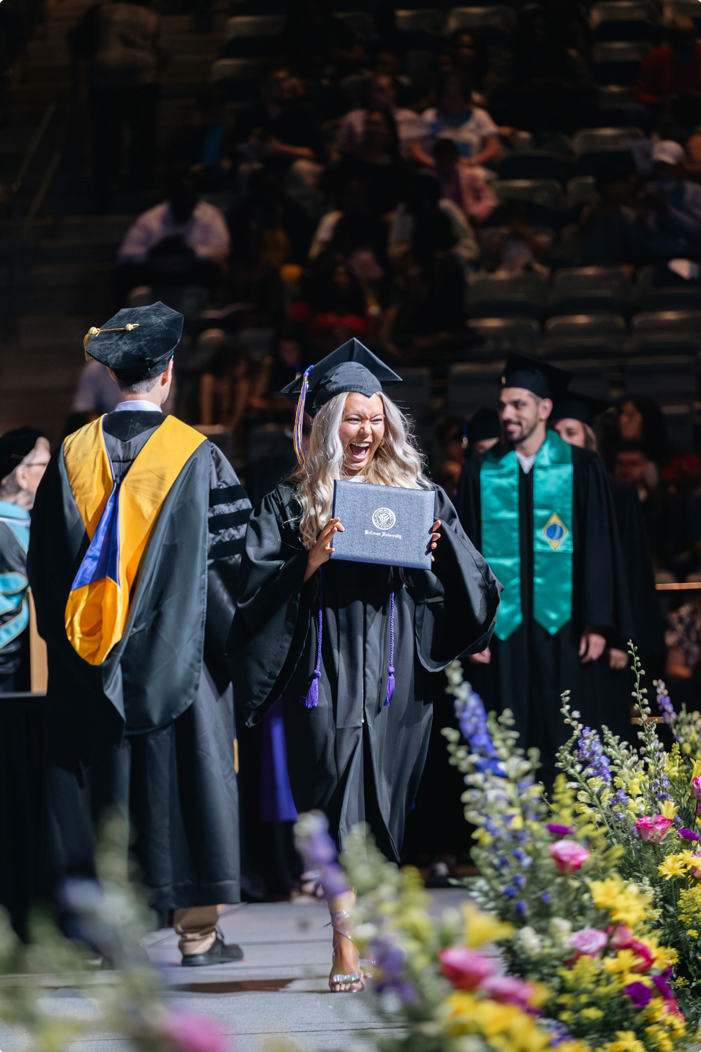 Woman in cap and gown smiling as she receives her diploma.