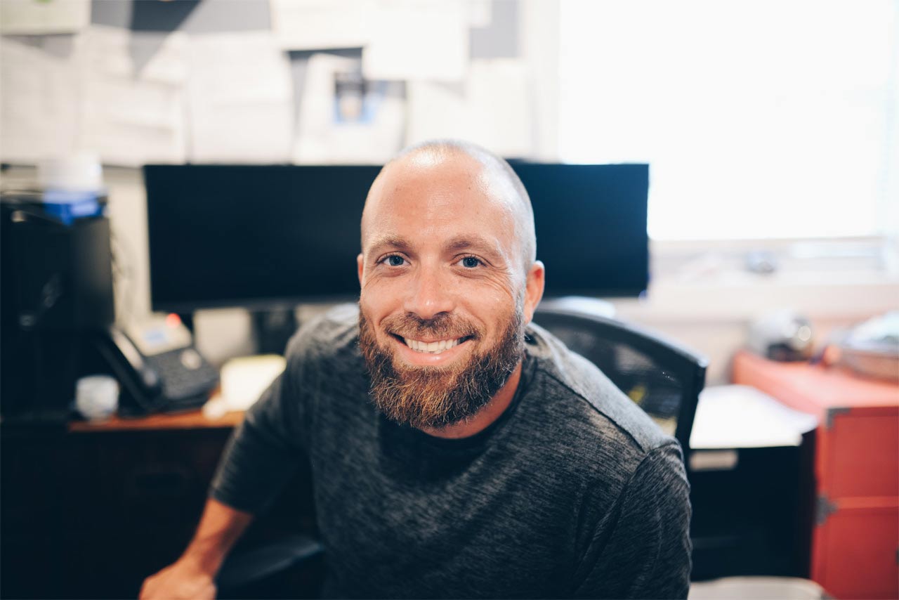 man at work desk smiling at camera